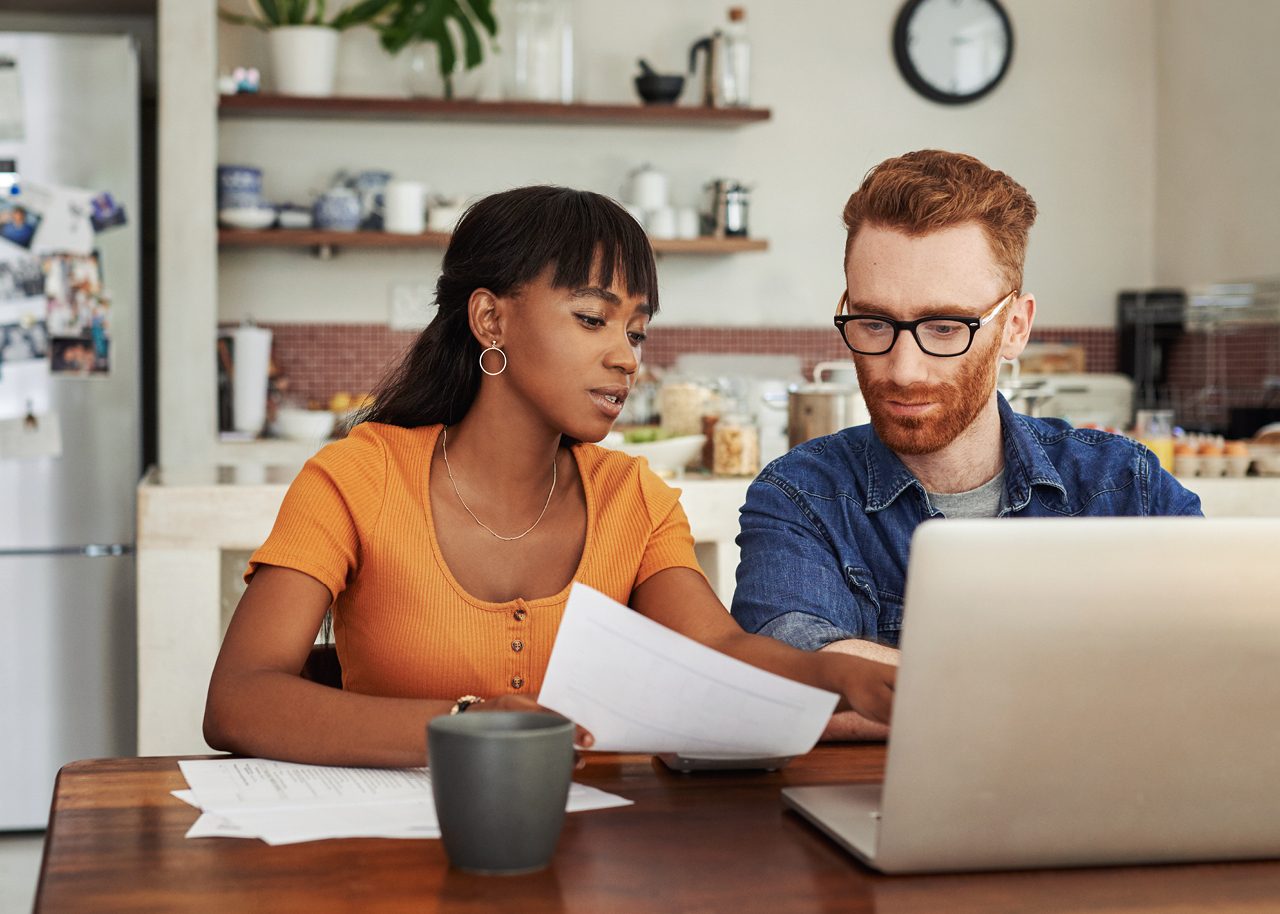 Adult couple sitting at kitchen table and looking at papers and laptop